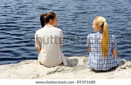two friends sit near the lake and enjoy an afternoon outdoors together