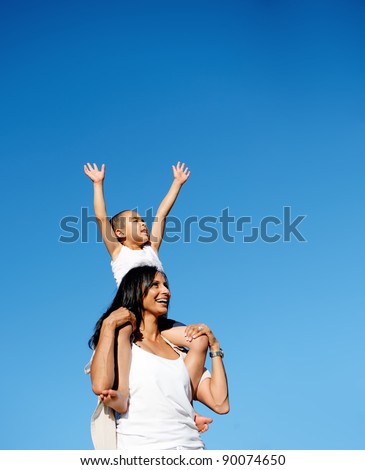 young boy sits on his moms shoulders and reaches for the sky