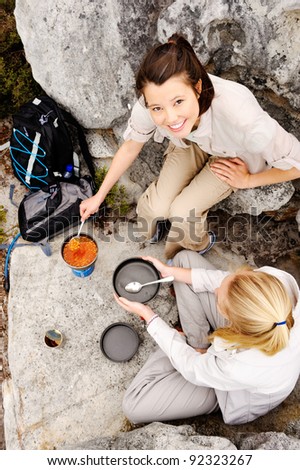 two friendly women cook up some food while camping in the wilderness. outdoor hiking lifestyle concept