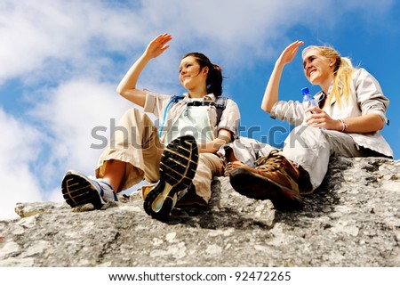 two women take a break from trekking and rest on a rock outdoors