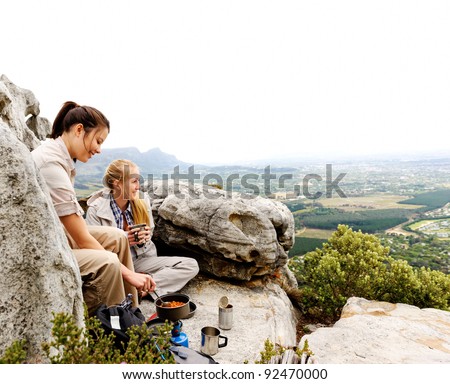 two friendly women cook up some food while camping in the wilderness. outdoor hiking lifestyle concept