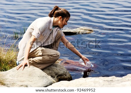 hiking woman fills up her water bottle in a fresh water lake