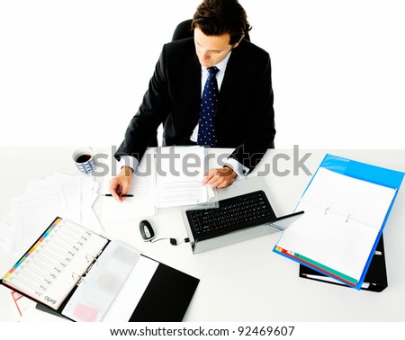 Man in business suit reads some documents at his desk full of files and a laptop computer