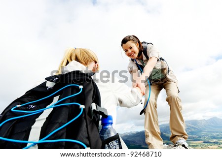 Hiking woman helps her friend climb onto the rock, outdoor lifestyle concept