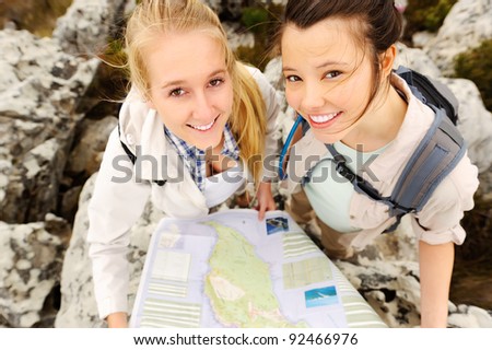 two cheerful women hiking outdoors and consulting their map for the direction in which to travel