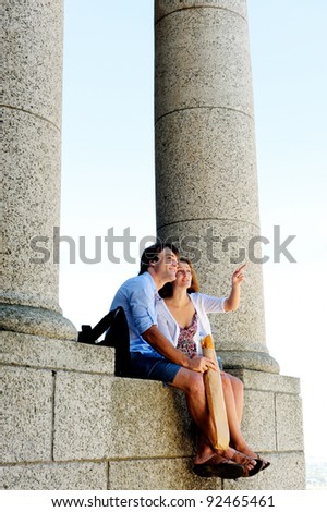 girlfriend points something out to her boyfriend and travel partner as they sit on the edge of an ancient temple
