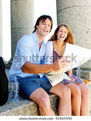 couple hold map and smile towards camera while sitting at an old tourist attraction. young travel concept