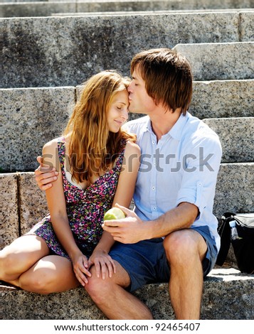 A couple traveling sit on the steps of a local landmark and kiss in the afternoon sunlight