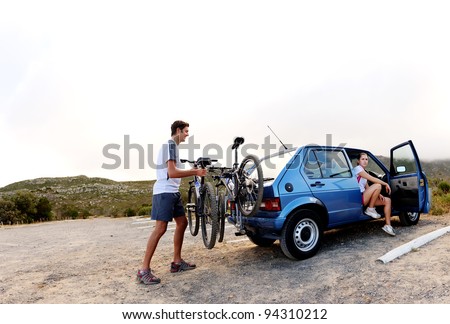 Panorama of a couple who have finished mountain biking outdoors and are loading the bicycles onto the car bike rack. large image, lots of copyspace, healthy lifestyle scene.