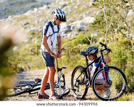 Bicycle has flat tyre and man helps his girlfriend pump it up. outdoors mountain bike couple.