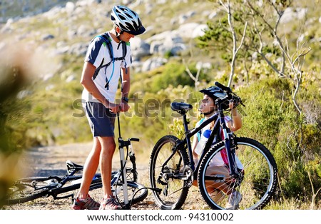Bicycle has flat tyre and man helps his girlfriend pump it up. outdoors mountain bike couple.