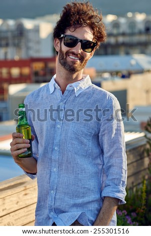 portrait of young man standing outdoors on rooftop terrace with beer