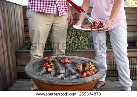 Women helping at the outdoor barbeque with a plate while man serves healthy chicken kebabs