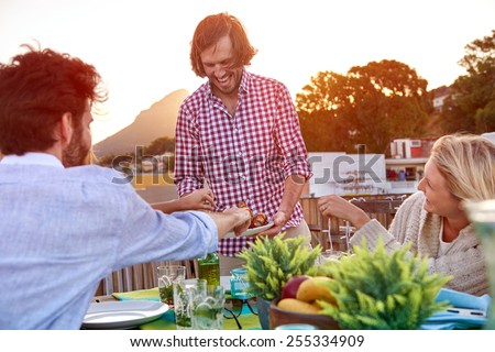Man serves friends skewer kebabs at outdoor rooftop barbeque dinner party