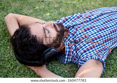 man listening to music relaxing on green grass outdoors in summer