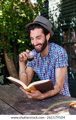young man relaxing outdoors reading literature novel story book with glass red wine at home