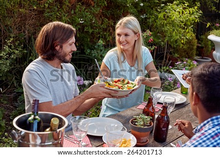 woman passing fresh healthy salad at outdoor friends dinner party gathering