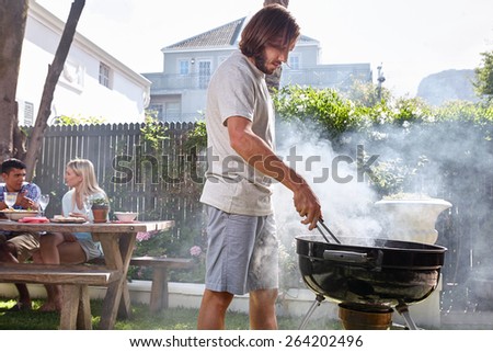 young man preparing fire for friends outdoor barbecue garden party