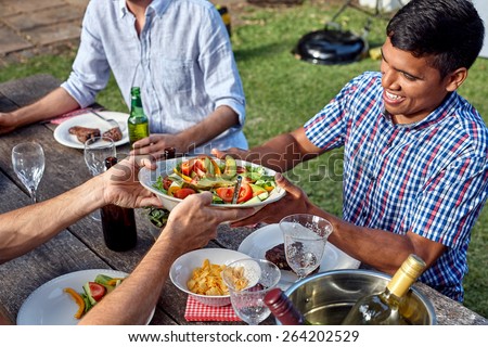 man passing dish healthy fresh salad at outdoor barbecue garden party gathering
