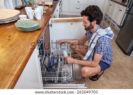 man packing dirty dishes into dishwashing machine in home kitchen