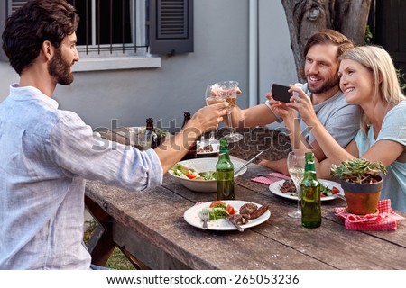 group of friends drinking cheers taking picture photos on mobile cellphone camera at outdoor garden party