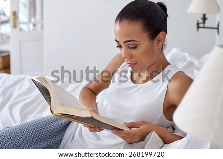 young woman relaxing on bed reading literature novel story book at home