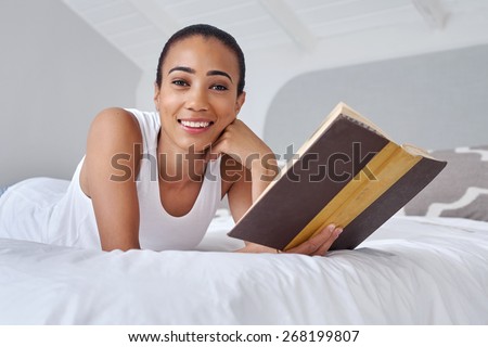 young woman laying relaxing on bed reading literature novel story book at home
