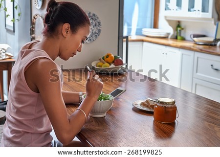 young woman enjoying healthy salad bowl with mobile cellphone at home kitchen