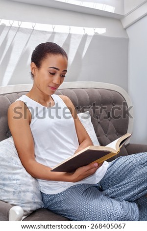 young woman relaxing on sofa couch reading literature novel story book sitting at home living room lounge
