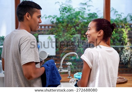 young woman washing dirty dishes while husband dry off in kitchen