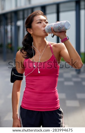asian chinese sporty woman outdoors quenching her thirst with water bottle during morning workout