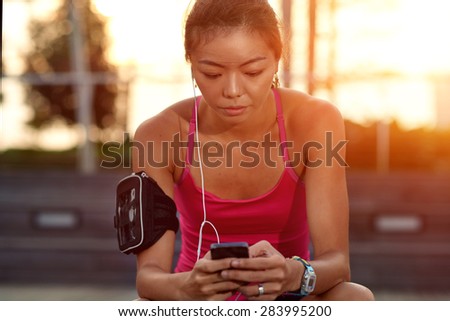 asian chinese woman with mobile phone choosing music for morning workout fitness run