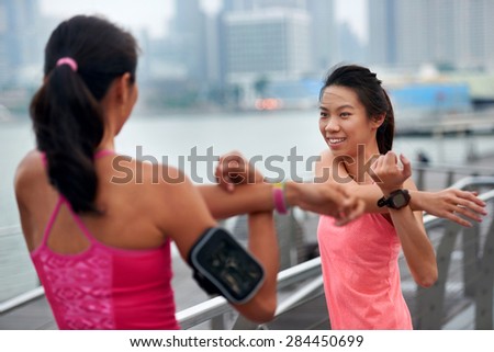 sporty asian chinese women doing stretching exercise outdoors along city sidewalk