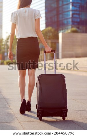 travel business woman pulling suitcase bag walking along sidewalk outdoors in urban city