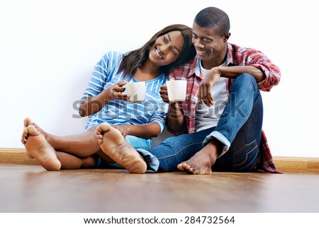 Young african couple sitting on floor of new home with coffee and being happy with life success of property investment