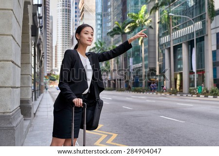 traveling asian chinese business woman calling for taxi cab from city street sidewalk
