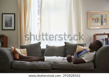 african black man sleeping on sofa couch while reading book at home living room lounge