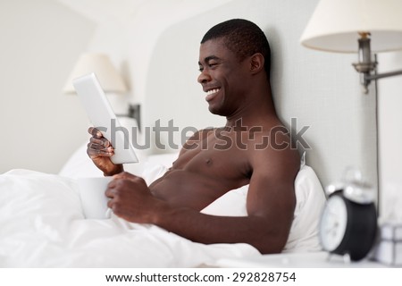 handsome african black man with tablet computer sitting comfortably in bed at home