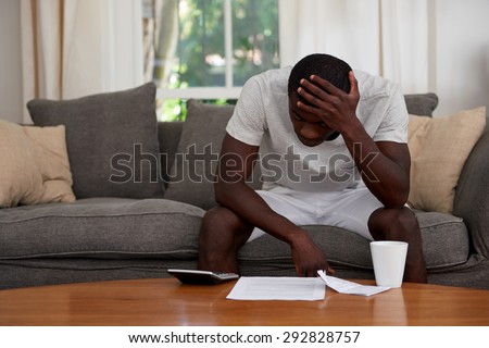 disapointed troubled african black man sitting on sofa couch calculating home bill finance debt in living room