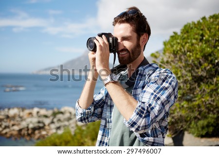 young, attractive caucasian man standing and taking pics of the ocean using a digital camera