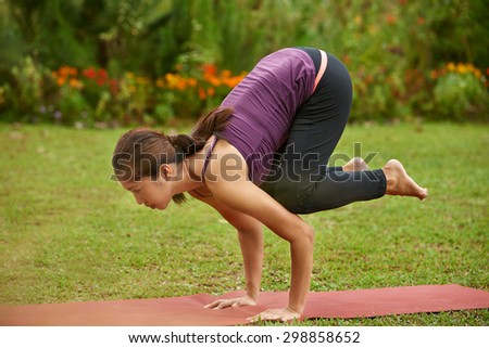 Young woman in the park doing yoga pose arm balance crow pose