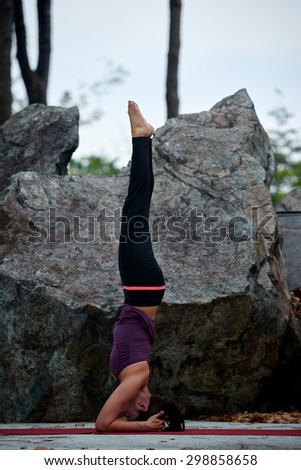 young fitness woman practicing yoga poses near rocks head stand