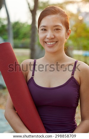 portrait of young smiling fitness yoga woman holding a yoga training mat