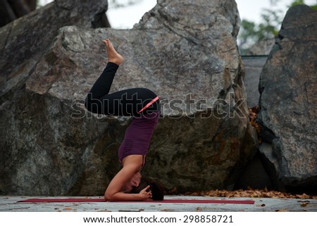 young fitness woman practicing yoga poses near rocks head stand
