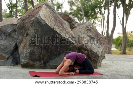 young fitness woman practicing yoga Pigeon Pose Kapotasana near rocks