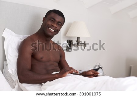 portrait of handsome african black man with tablet computer sitting comfortably in bed at home