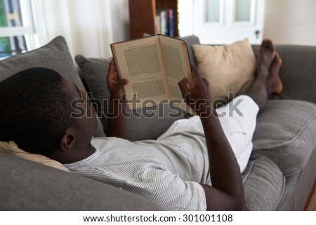 intelligent african black man relaxing on sofa couch reading literature novel story book at home living room lounge