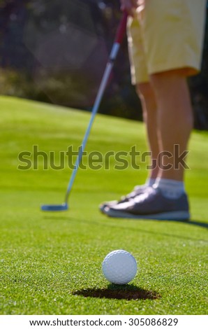 Golfer putting golf ball to hole