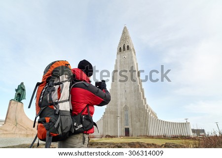 rear view adventure travel backpack man taking pictures of the Hallgrimskirkja cathedral in reykjavik iceland