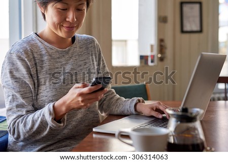 Asian Chinese woman busy reading text while working on laptop at breakfast coffee